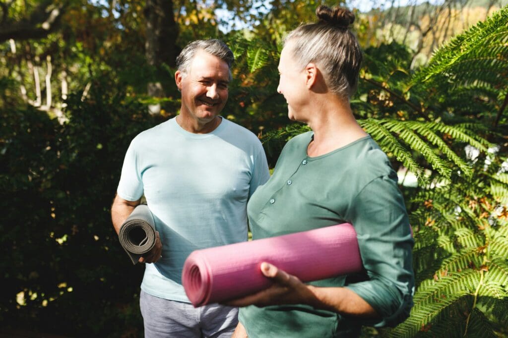 Happy senior caucasian couple practicing yoga, holding yoga mats in sunny garden